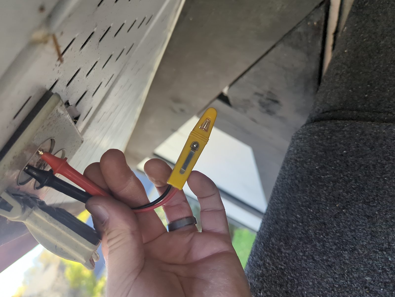 A hand holding a yellow tester on a connector at the side of the house.