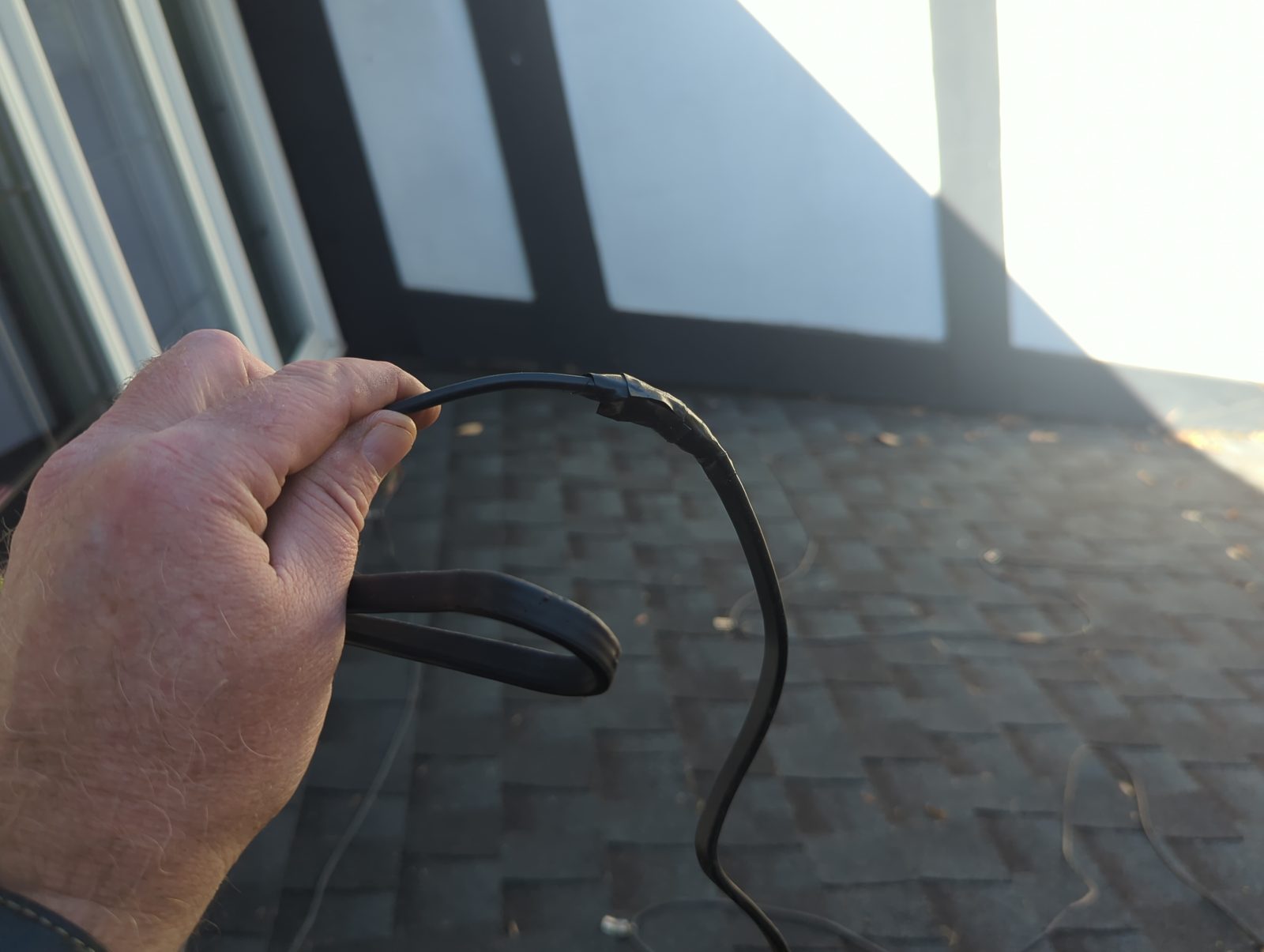 A damaged black cable held over roof shingles.